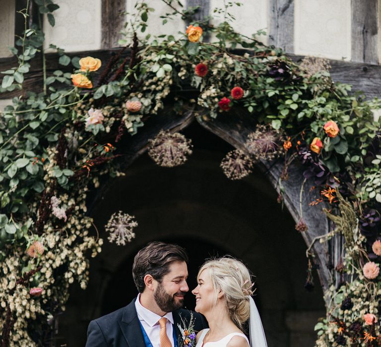 Bride and groom in classic wedding attire standing outside the church with floral arch decor 