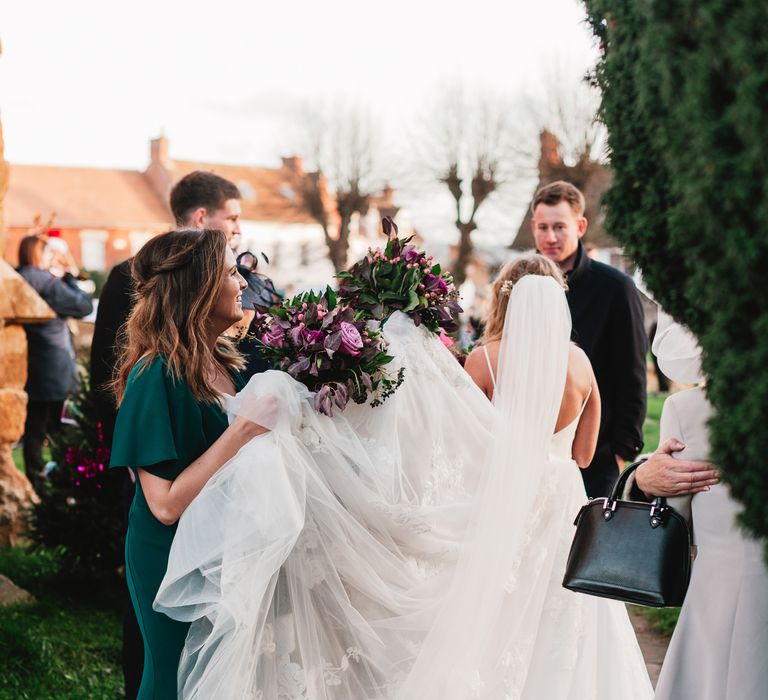 Bridesmaid helps bride with her veil and dress outside