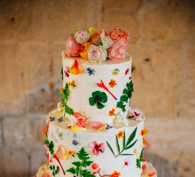 Three tier wedding cake with pink, yellow orange, green and peach botanical detail with peach wedding roses on top