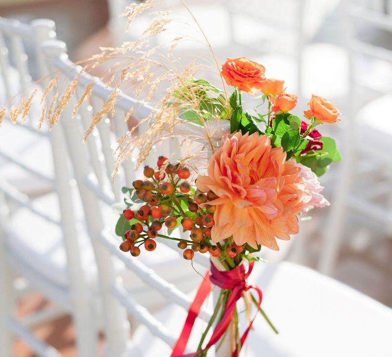 Orange dahlia flower with red berries and ribbon decorating the aisle seating