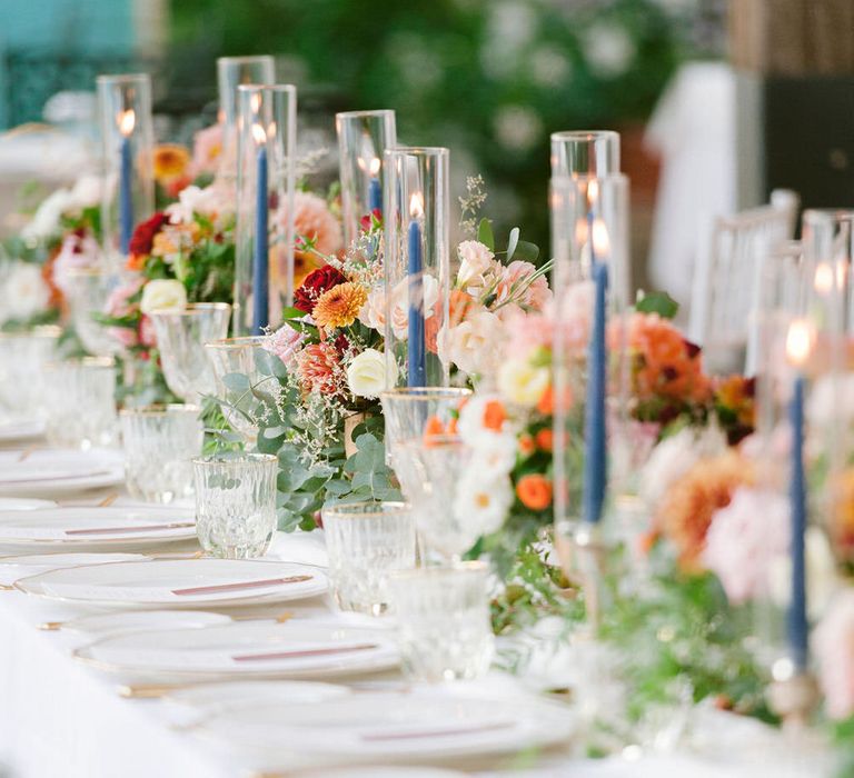 Blue tapered candlesticks with orange floral centrepieces of roses, dahlias and eucalyptus leaves