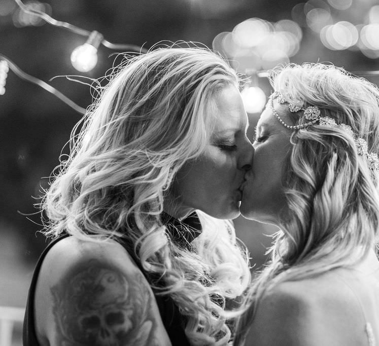 The brides share a kiss at their evening wedding reception