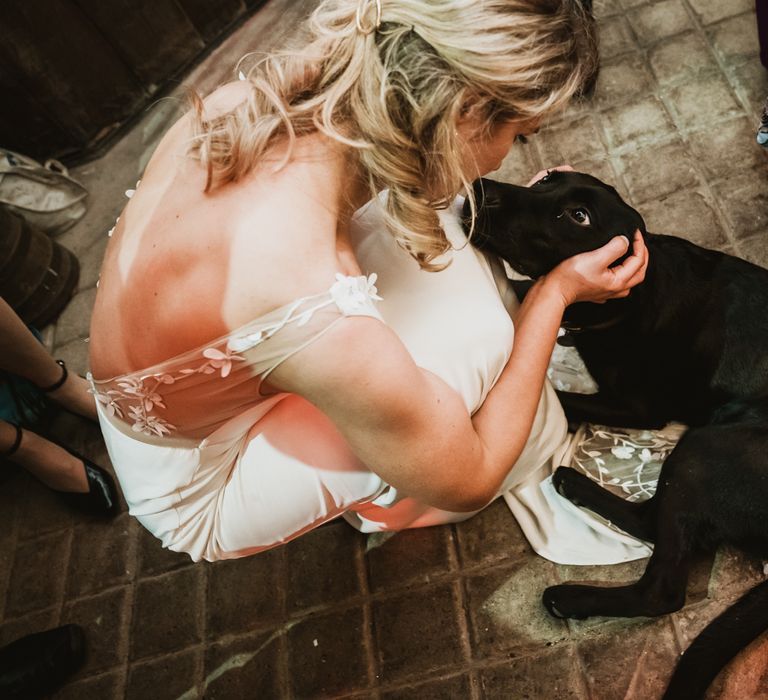 Bride sits down to stroke black Labrador dog 