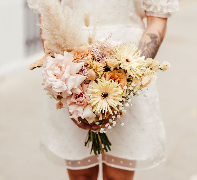 Bride holding a pastel pink, orange and yellow wedding bouquet 