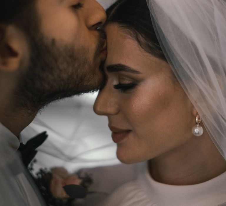 Groom kisses the forehead of his bride as she looks down and slightly smiles