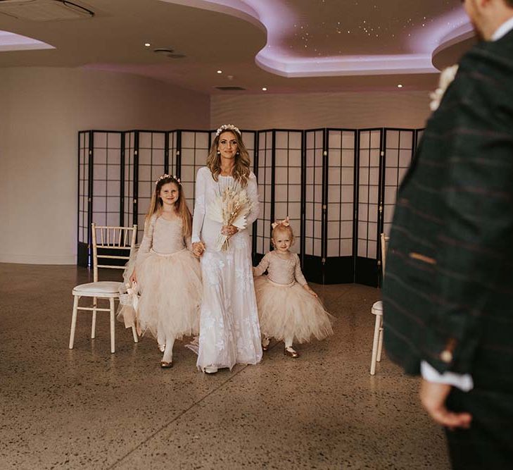 Bridal entrance at Seaside elopement with bride in a long sleeve lace dress walking down the aisle with her two daughters in Tutus 