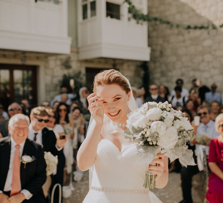 The bride smiling at the top of the aisle holding her white wedding bouquet