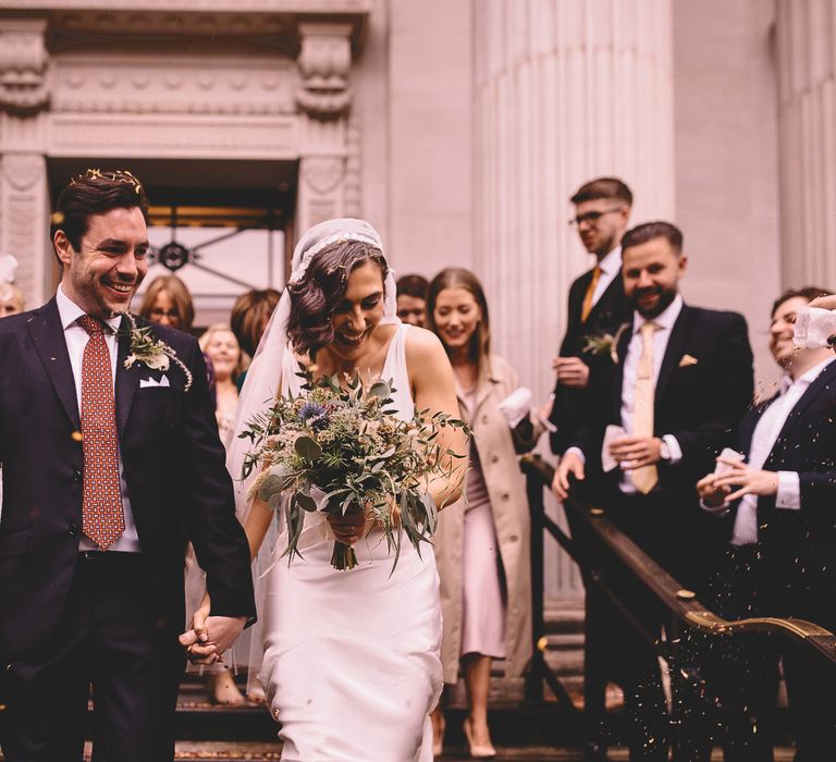 Old Marylebone Town hall confetti exit with bride in a Juliet Cap veil holding a blue, white and green foliage bouquet 