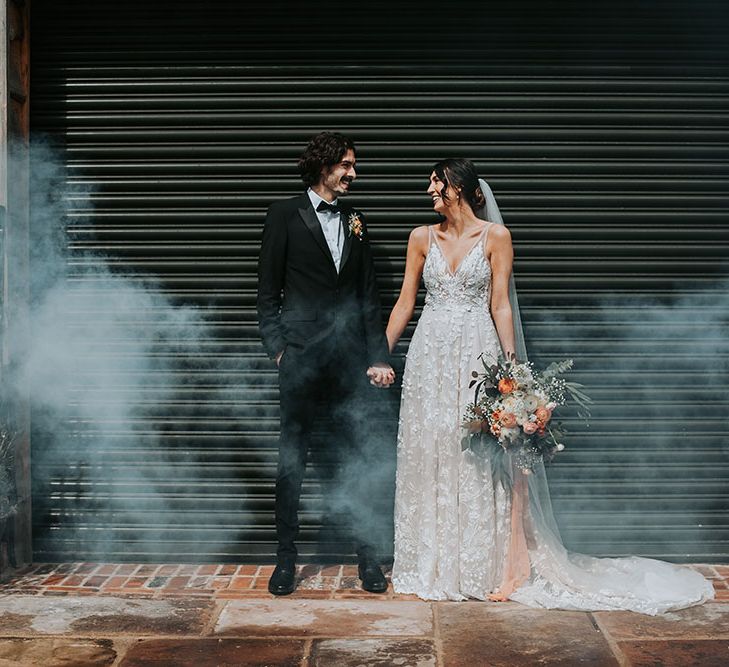 Smoke bomb portrait with bride in an appliqué wedding dress and groom in a black tie suit and bow tie 