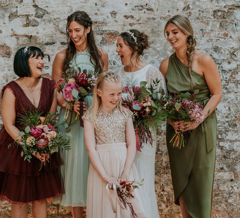 Bride stands with her bridal party who wear different coloured and styled bridesmaid dresses with brightly coloured floral bouquets