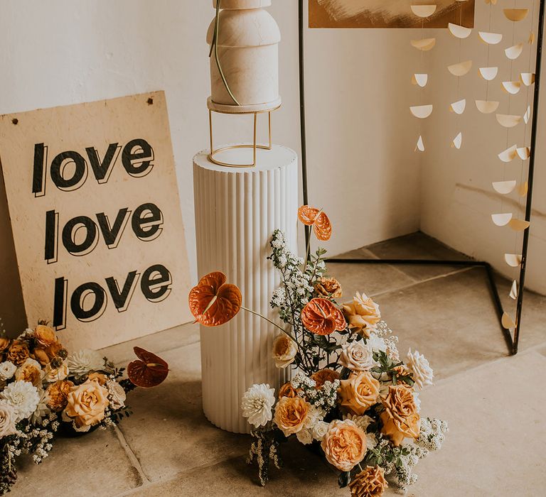 Wedding decor with metal frame and hanging sign, orange and yellow wedding flowers and tall wedding cake on a cake stand 