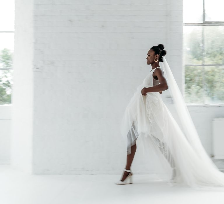 Beautiful black bride with afro hair in a princess wedding dress and cathedral length veil walking though an industrial wedding venue 