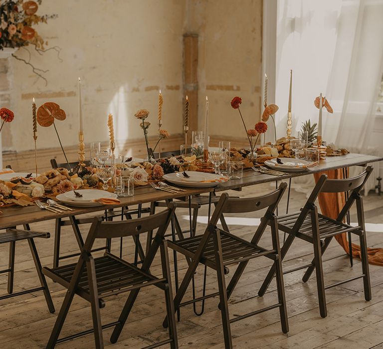 Orange and rust coloured wedding table decor with grazing boards, taper candles, and single stem dahlias and anthuriums 