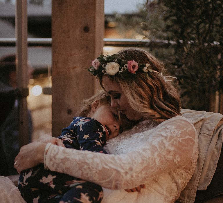 Bride in a long sleeve wedding dress hugging her daughter during the back garden evening reception 