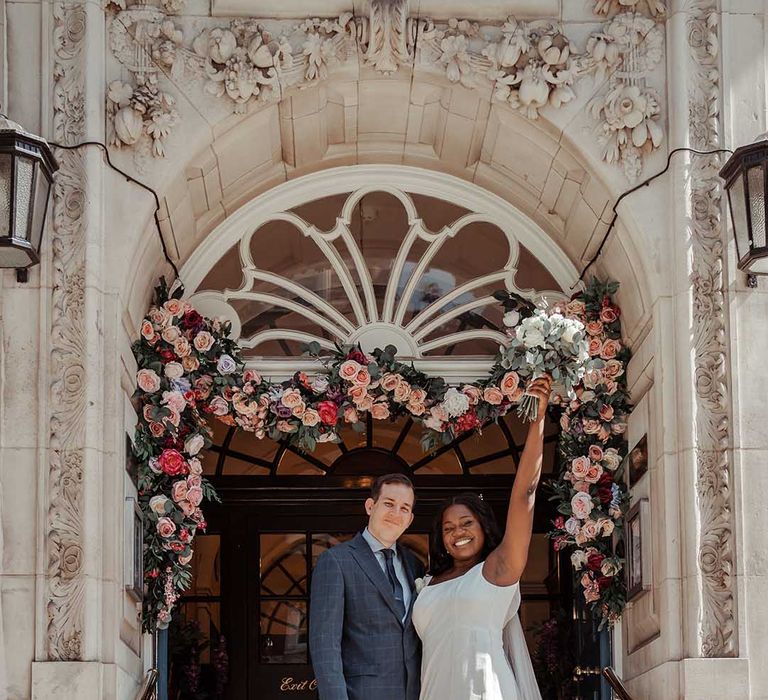 Bride lifts her bouquet in the air in celebration after Chelsea Old Town Hall wedding ceremony