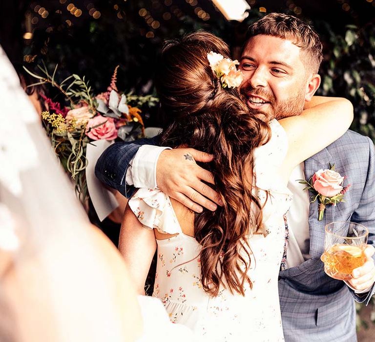 Bridesmaid hugs groom in blue check suit after the Stone Barn Cotswolds wedding ceremony 