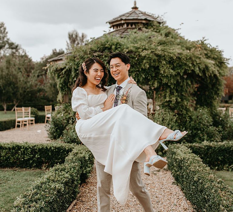 East Asian bride is carried by her groom down pathway on her wedding day