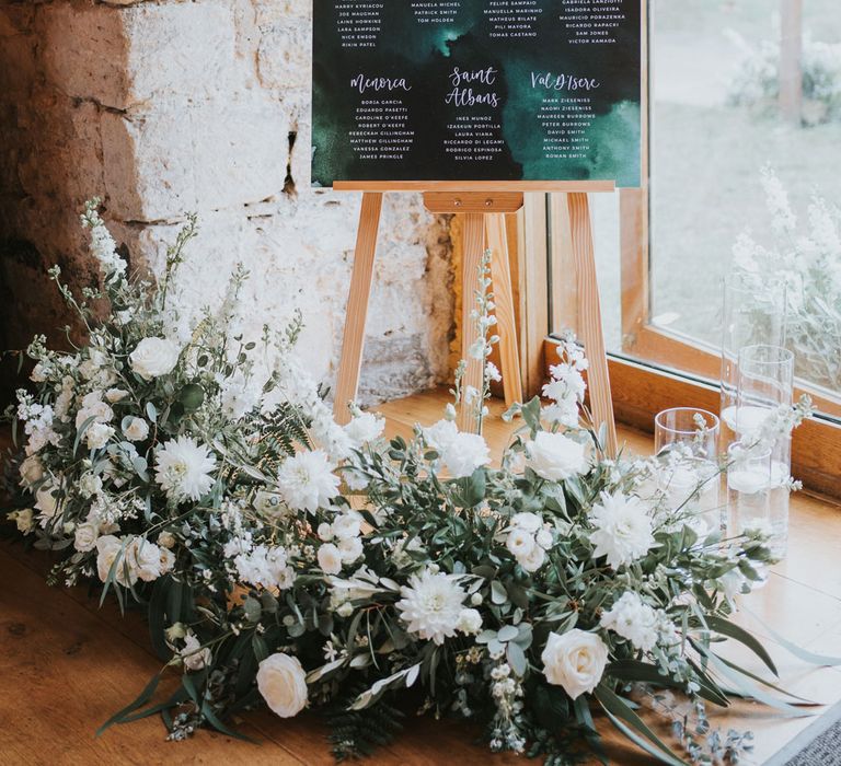 Green acrylic wedding table plan on wooden easel with white and green floral garland and candles for elegant wedding at Notley Abbey