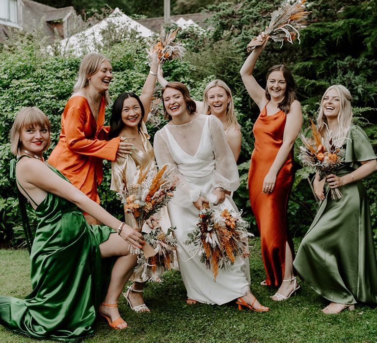 Bride in a long sleeves wedding dress with sheer sleeves and bridesmaids in green and orange satin bridesmaid dresses 