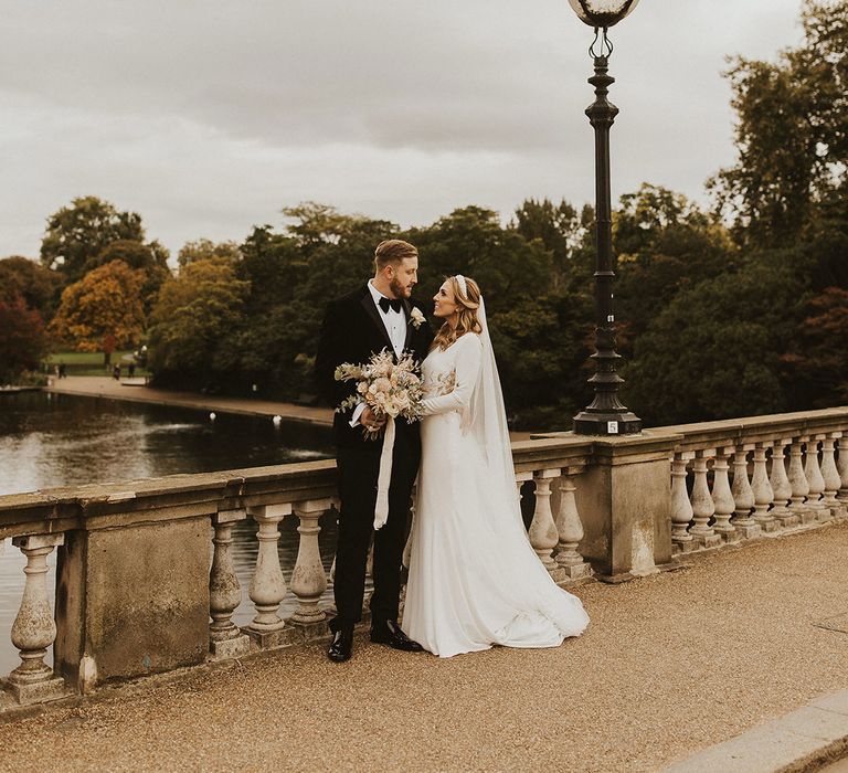 Elegant LONDON, city wedding with bride and groom posing on a bridge over the Thames in a tuxedo and fitted wedding dress with long sleeves