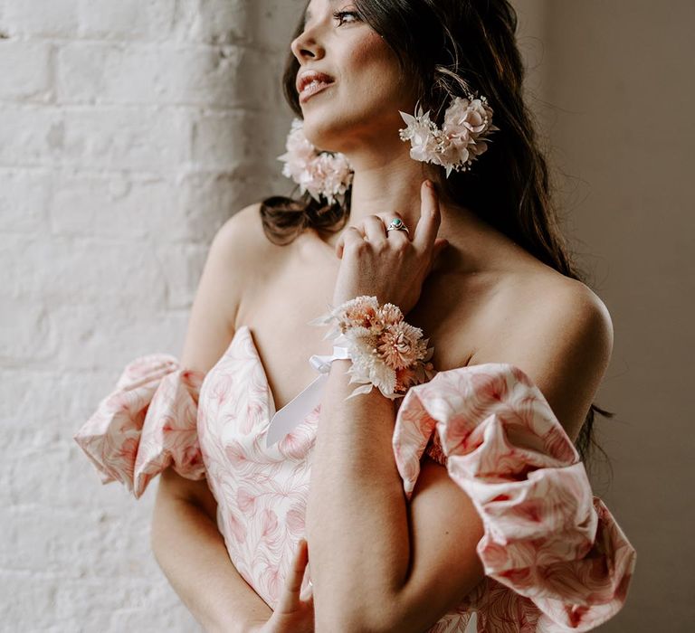 Bride in pink patterned bridal separates with puff sleeves wearing a dried flower wrist corsage and matching hoop earrings 