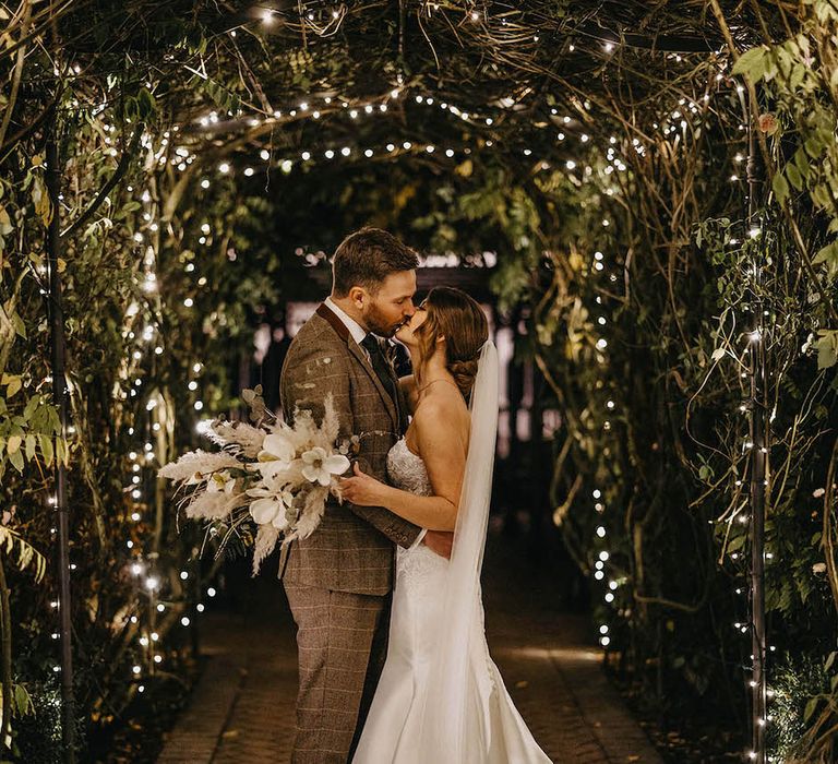 Bride and groom kiss under fairy lights