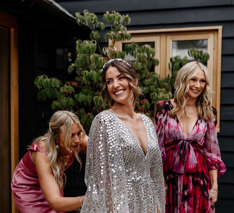 Bridesmaid in a pink dress helping the beautiful bride into her silver sequin wedding dress 