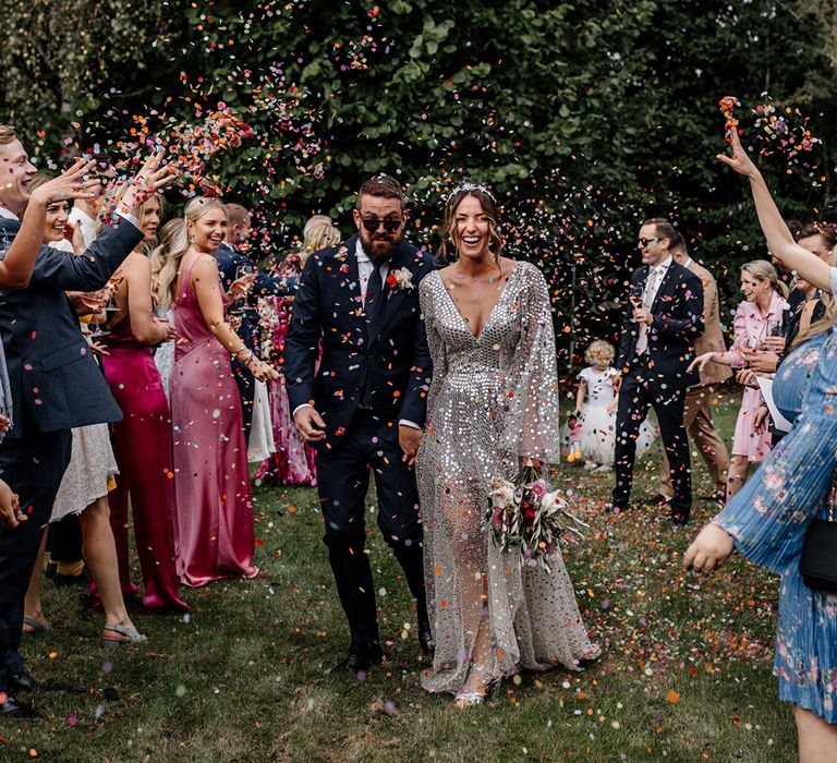 Colourful confetti moment with bride in a silver sequin wedding dress and groom in a navy suit at back garden wedding 