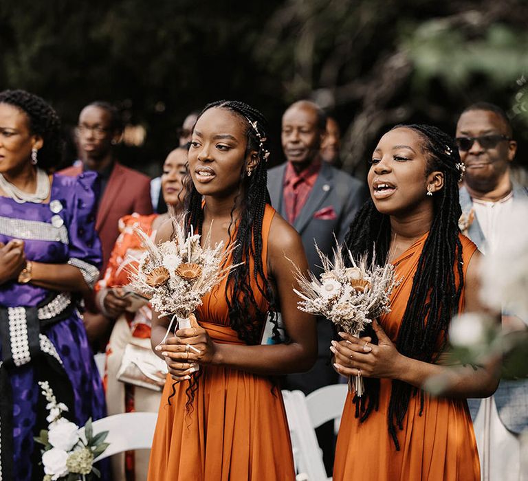 Bridesmaids wear multiway bridesmaids gowns in orange with dried floral bouquets