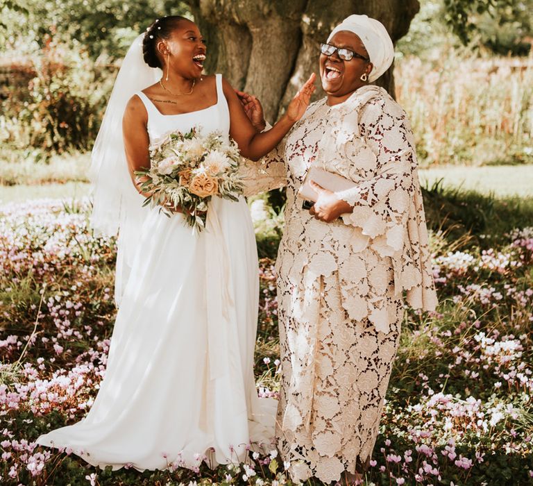 Black bride and mother of the bride laughing together under a tree at Elmore Court 