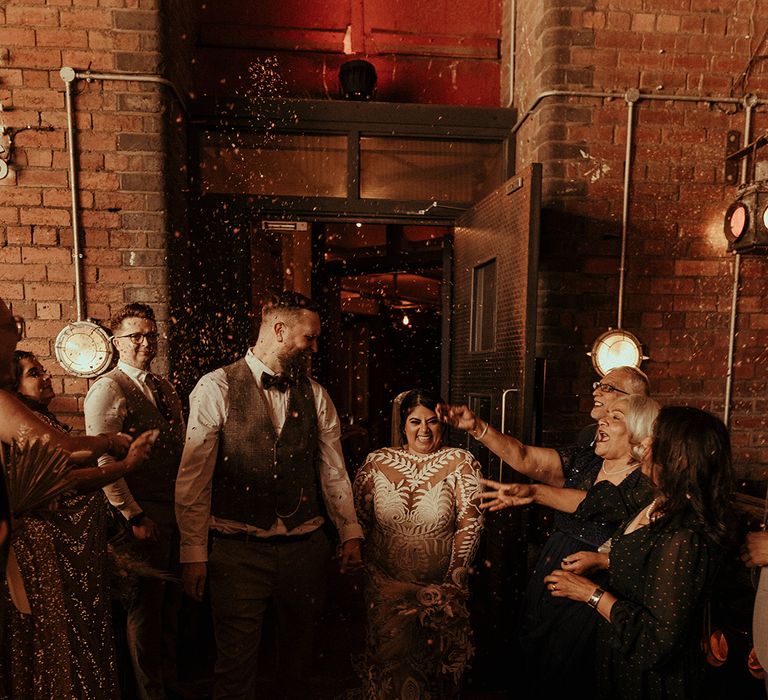 Confetti moment at Victoria Warehouse wedding with groom in a tweed waistcoat and trainers and bride in a long sleeve lace wedding dress