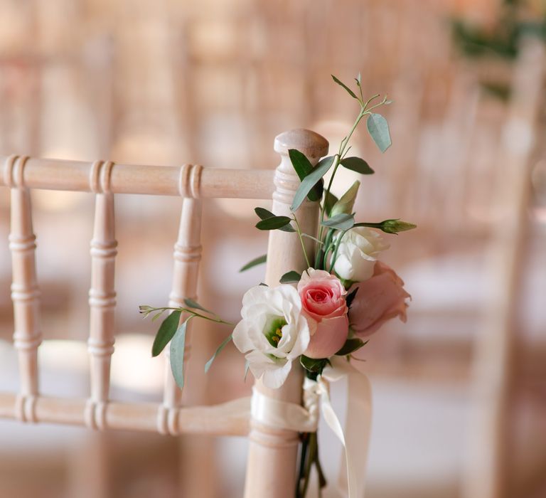 Pastel flowers tied to wooden chair with white ribbon