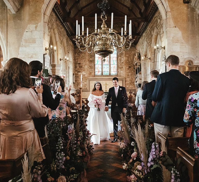 Bride and groom walk back down the aisle as a married couple at church wedding ceremony 