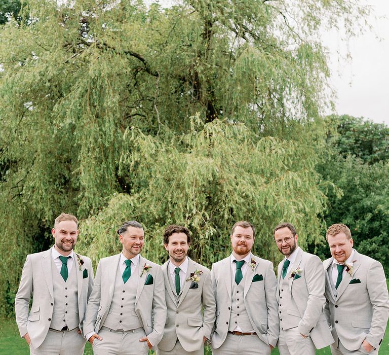 Groomsmen in matching light grey three piece suits with matching green ties and handkerchiefs