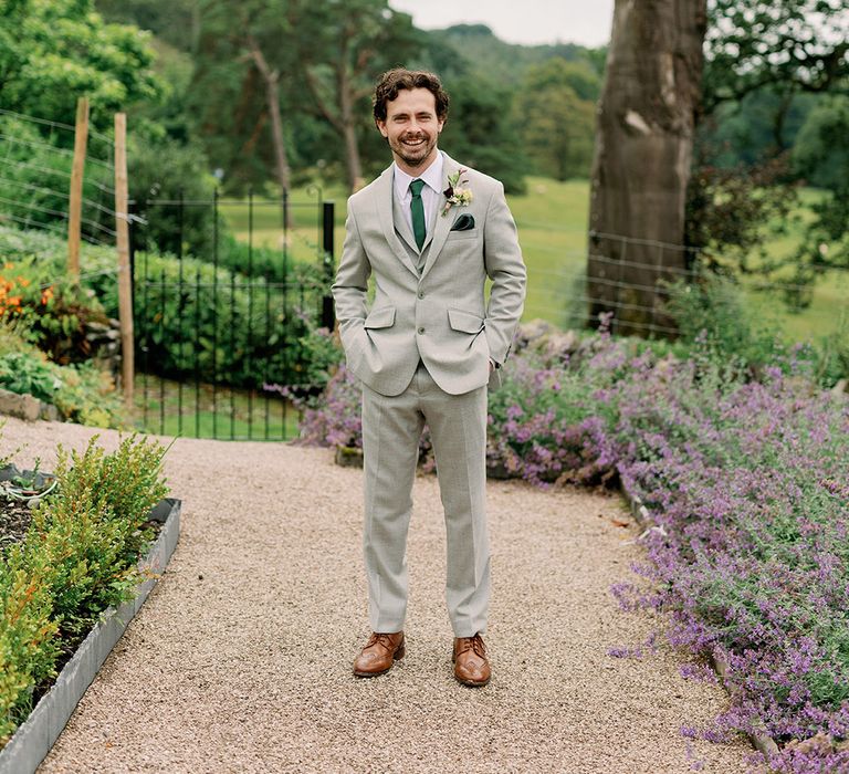 Groom solo shot in bespoke light grey three piece suit and forest green tie and handkerchief with flower buttonhole 