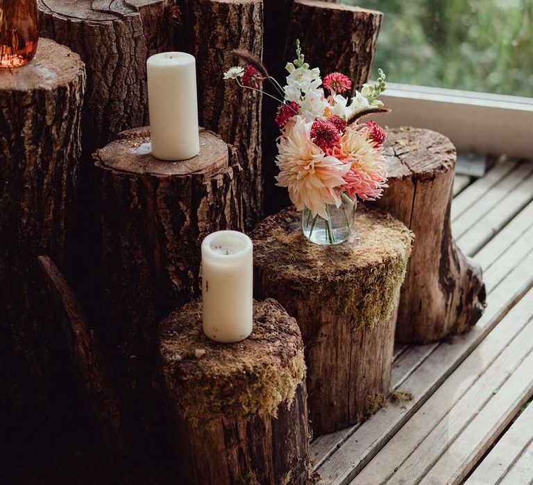 Wedding decor with tree trunks and white pillar candles with pink, red and white flowers 