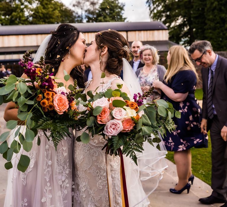 Brides share a kiss after having their confetti exit from their wedding ceremony