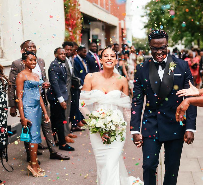 Smiling bride and groom exit their wedding ceremony to multi-coloured confetti exit 