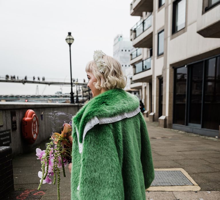 Bride with short blonde hair and white flower headband wearing green fur coat with velvet platform block heels