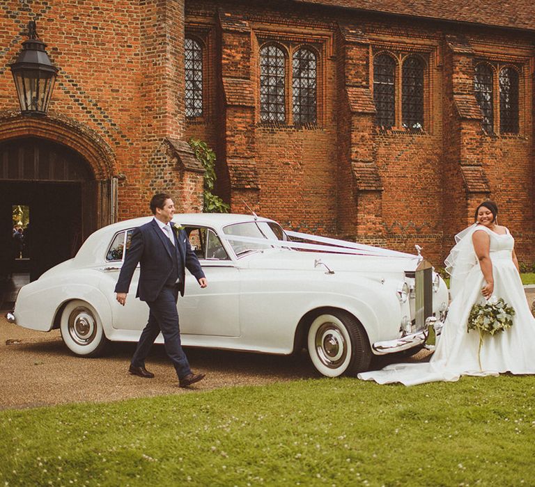 Bride and groom pose in front of their white wedding car transport 