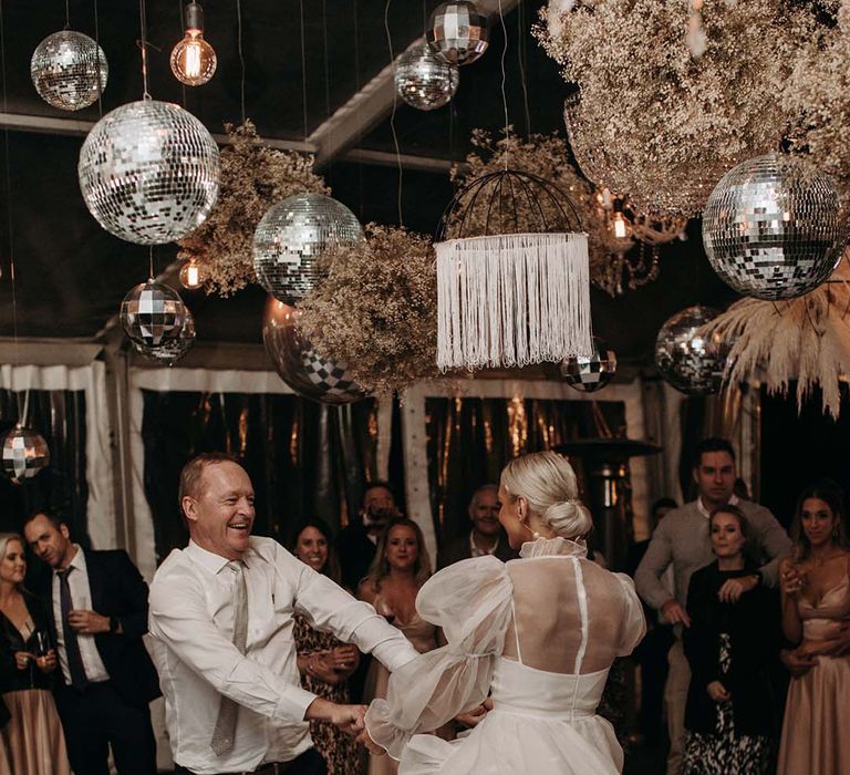 Bride in a short wedding dress dancing at her evening reception with her groom under a canopy of disco balls 