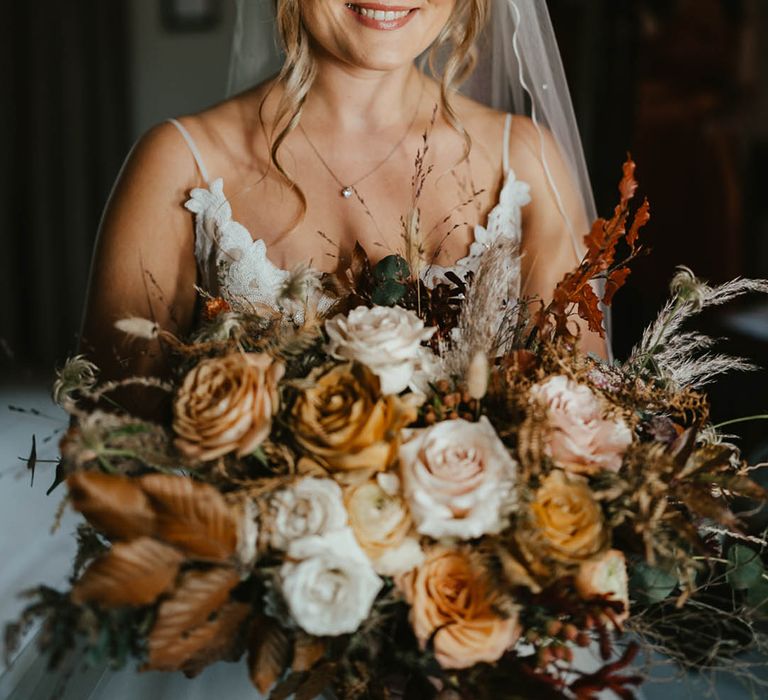 Bride with warm toned eyeshadow holding matching warm-toned autumnal wedding bouquet for her autumn wedding 