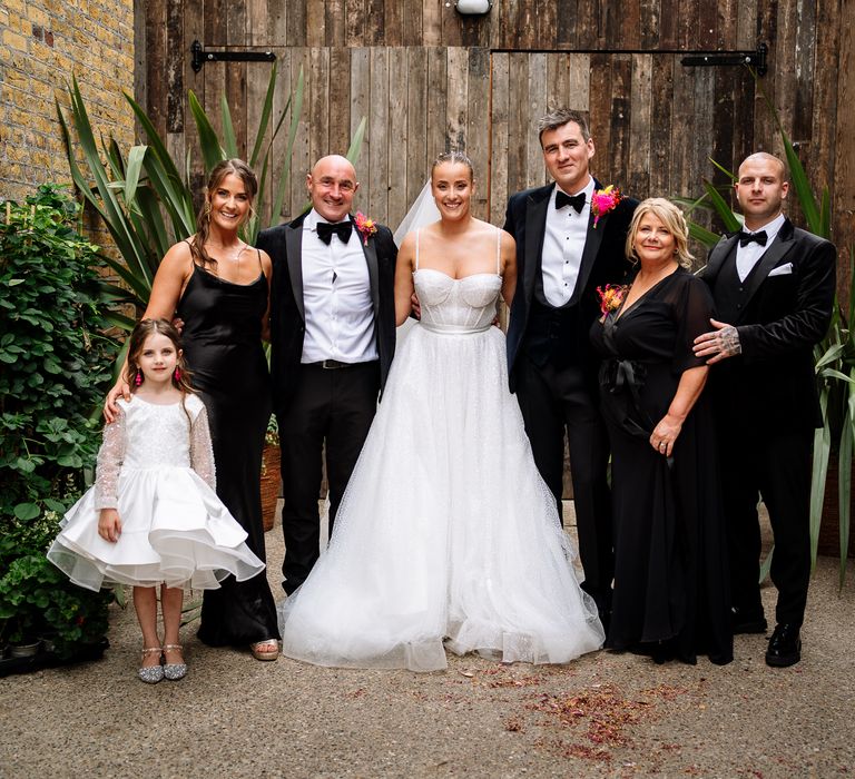 Bride & groom stand beside family members in black tie and flower girl in short ballerina styled dress 