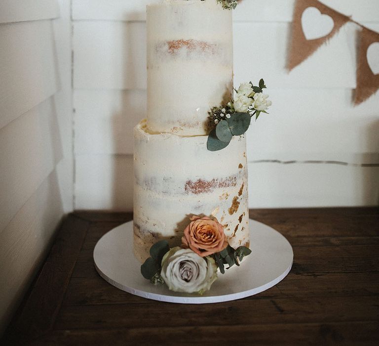 Two tier naked frosted wedding cake complete with white floral decor