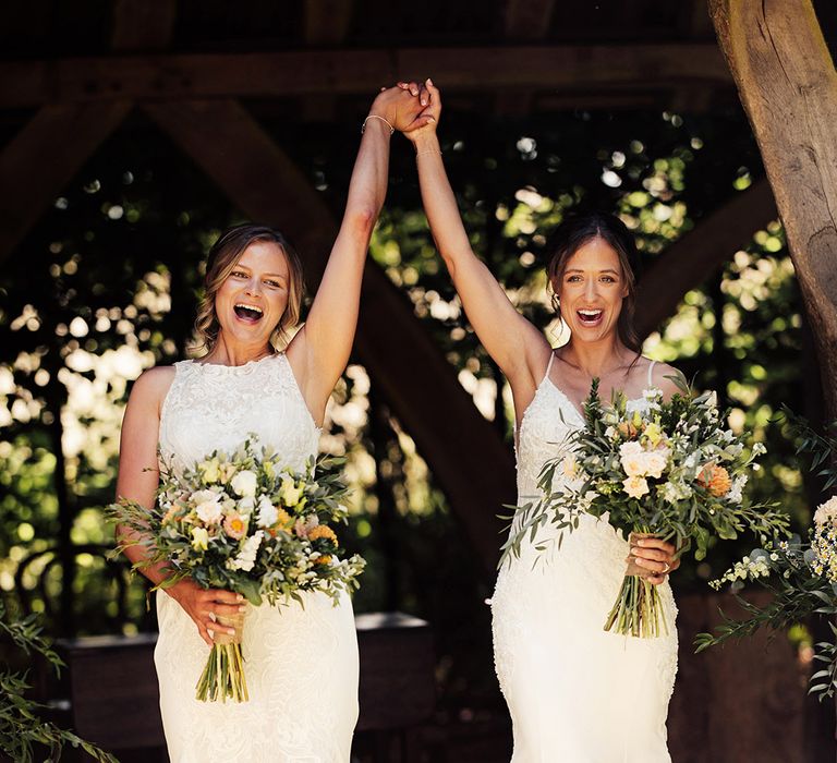 Brides raise their joint hands as they turn to face their guests as a married couple after their outdoor wedding ceremony 