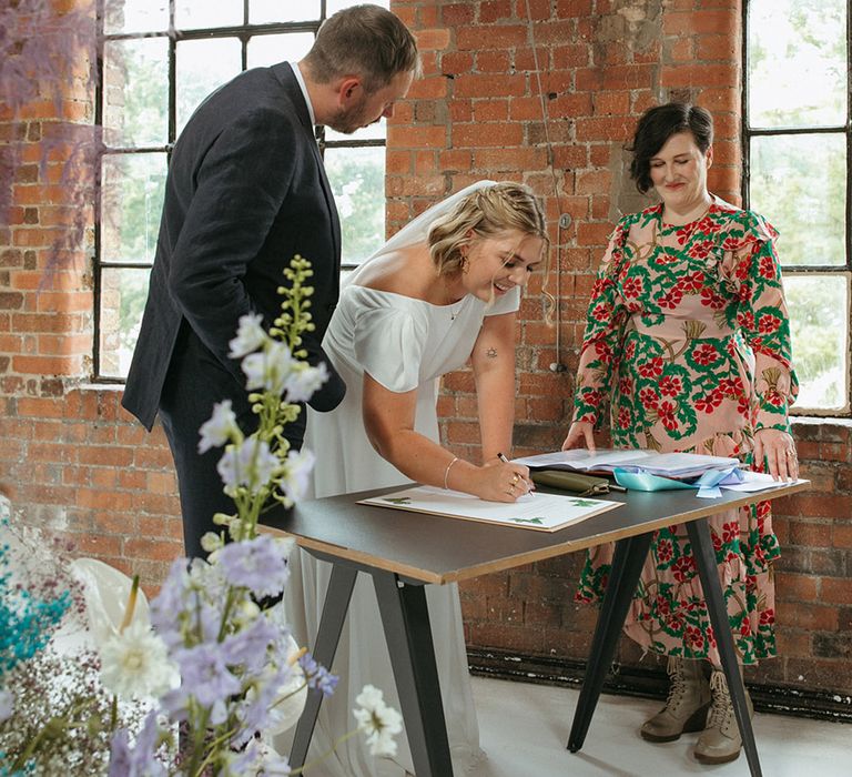 The bride and groom sign the wedding register as their celebrant watches