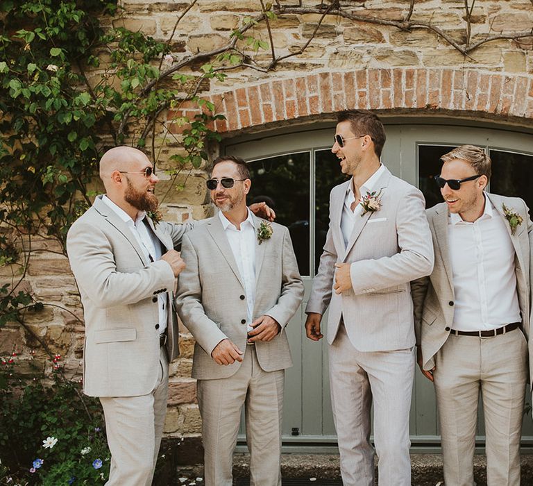 Groom smiles with the groomsmen as they all wear sunglasses and matching pale suits 