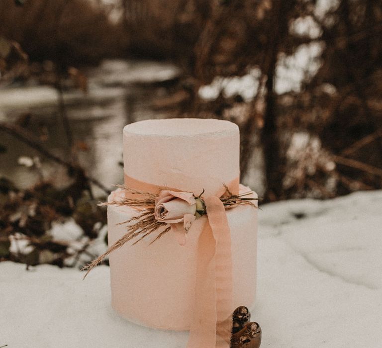 Two tier blush pink wedding cake out in the snow 