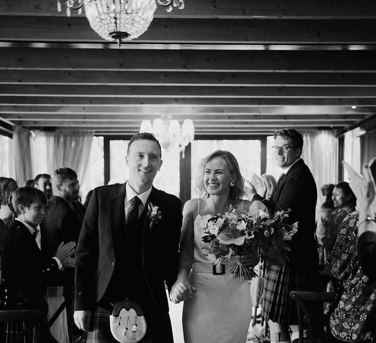 Bride in silk slip wedding dress walks alongside her groom in kilt after wedding ceremony at Shortflatt Tower