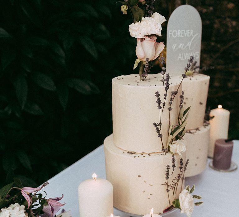 White and lavender pillar candles with three tier buttercream cake with lavender and white rose decorations